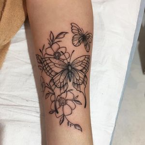 Elegant blackwork tattoo by Natalie Lucia featuring a delicate butterfly and flower design on the forearm. Intricate and stunning!