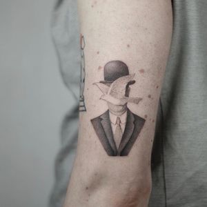 Intricate black and gray tattoo of a man in a suit and hat with a bird, beautifully illustrated by Dawid Szubert on the upper arm.