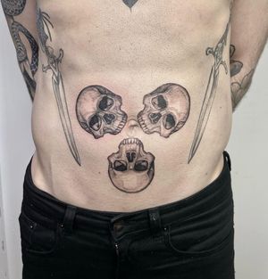 Illustrative black and gray design featuring multiple skulls, expertly done by Lou. W. Perfect for your stomach area.