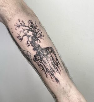 An illustrative black and gray tattoo of a tree with intricate roots, expertly done by tattoo artist Lou. W.