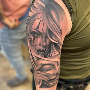 Captivating black and gray upper arm tattoo featuring a stunning realism woman wearing a clown mask by talented artist Phillip Wolves.