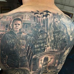 A haunting black and gray tattoo featuring iconic horror characters and elements like Michael Myers, Jason Voorhees, and Freddy Krueger, beautifully rendered in a realistic illustrative style on the back in Long Beach.