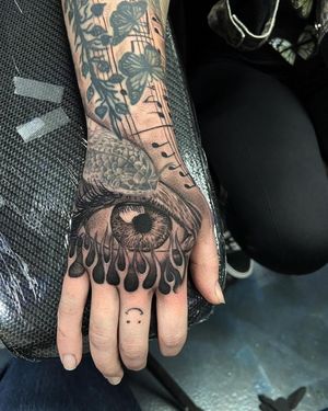 Get a captivating blackwork eye engulfed in realistic flames on your hand in Long Beach.