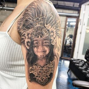 Capture the spirit of a Native girl with this stunning black and gray, illustrative feather tattoo on your upper arm in Long Beach, US.