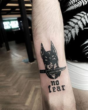 A unique forearm tattoo featuring a dog, knife, and powerful quote in bold blackwork style by the talented artist Lars.