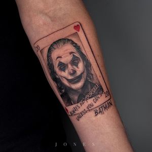 Unique forearm tattoo by Jones featuring a heart, joker, card, and casino quote in a mix of blackwork, fine line, and realism styles.
