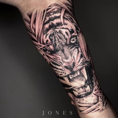 Impressive blackwork tattoo of a fierce tiger surrounded by intricate leaves, created by the talented artist Jones.
