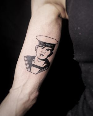 A stunning blackwork forearm tattoo by Lars featuring an illustrative design of a man wearing a cap with fine line and small lettering for a quote.