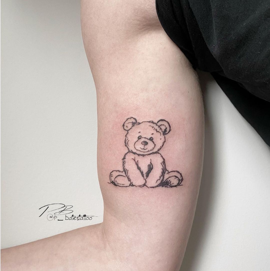 Line art teddy bear tattoo on the inner arm.