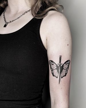 Illustrative blackwork tattoo of a butterfly and sword on upper arm, by Lars. Unique and bold design.