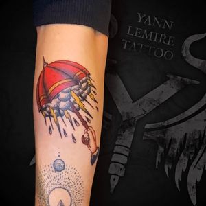 Colorful traditional tattoo featuring a hand holding an umbrella under rain clouds, beautifully executed by Yann on the forearm.