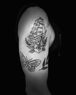 An illustrative blackwork tattoo featuring a beautiful butterfly, flower, and ship design on the upper arm, by artist Niklas Fogh.