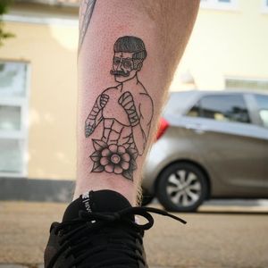 Unique blackwork design by Yura featuring a man boxing with gloves surrounded by a flower motif on the shin.