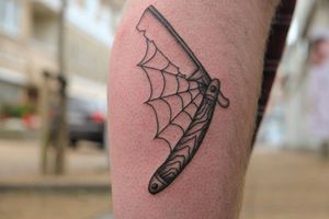 Illustrative lower leg tattoo featuring a spider, spider web, and razor, done by Yura. Perfect for a bold and edgy look.