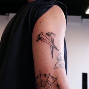 A striking blackwork tattoo of nails, beautifully designed by Yura, perfect for the upper arm.
