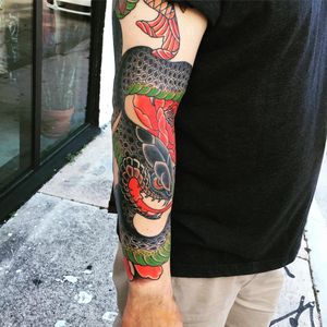 Intricate Japanese forearm tattoo featuring a snake and flower design by renowned artist Ami James. Exquisite detail and bold colors create a stunning statement piece.