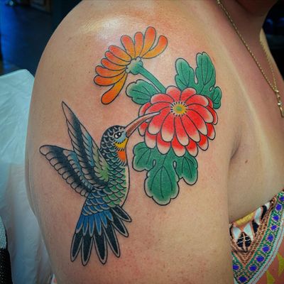 Eddy Ospina's illustrative design featuring a vibrant hummingbird and delicate flower on the upper arm.