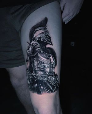 This black and gray tattoo by Marcel Oliveira features a detailed warrior wearing a helmet and armor, perfect for the upper leg placement.