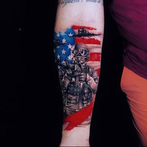Illustrative forearm tattoo featuring a gun, flag, soldier, and airplane, designed by Marcel Oliveira.