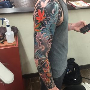Experience the beauty of Japanese craftsmanship with this intricate sleeve tattoo featuring koi fish, sakura flowers, and cherry blossoms by renowned artist Ami James.
