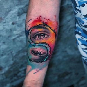 Vivid watercolor design by Marcel Oliveira, on the forearm, blending yin & yang symbol with an eye motif.