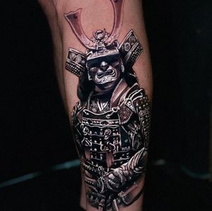 Bold blackwork design featuring a sword, samurai, and helmet on the lower leg. Created by tattoo artist Marcel Oliveira.