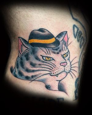 Unique tattoo design featuring a cat wearing a hat on the ribs, created by the talented artist Eddy Ospina.