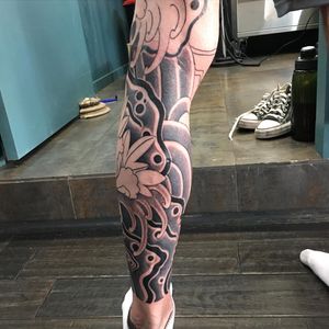 Beautiful illustrative tattoo by renowned artist Ami James, featuring a stunning combination of flowers and waves on the lower leg.