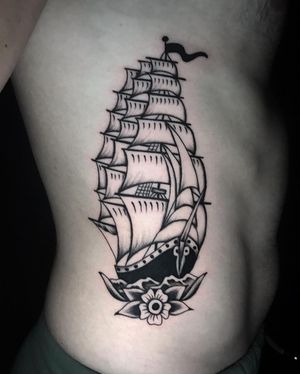 Dynamic blackwork design by Chris Tambo on ribs, combining traditional motifs of flowers and ships.