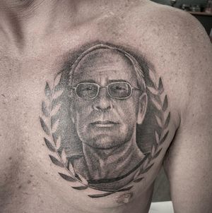 Capture the essence of sophistication with this black-and-gray chest tattoo featuring a man wearing glasses, accented with a sprig. By tattoo artist Rico Dionichi.