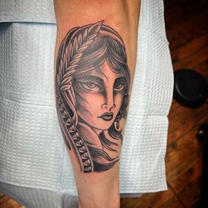 A stunning blackwork tattoo on the forearm featuring an illustrative woman with leaf earrings, done by the talented artist Darren Brass.