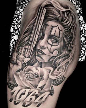 A stunning black and gray upper leg tattoo featuring a realistic chicano design of a flower, gun, woman, and year by talented artist Rico Dionichi.