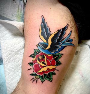 Stunning upper arm tattoo featuring a traditional style bird and flower motif by renowned artist Darren Brass.