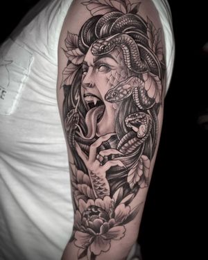 A striking blackwork tattoo on the upper arm featuring a snake intertwined with a flower and a woman, created by Rico Dionichi.