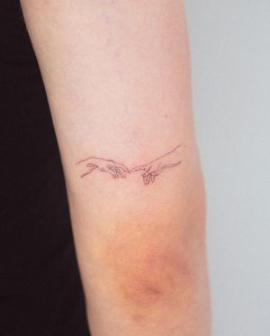 Gabriele Edu's illustrative tattoo of Michelangelo's hand on the upper arm, showcasing fine line craftsmanship.