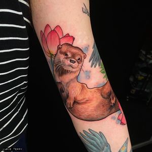 Stunning realism arm tattoo of a beautiful flower and playful otter by talented artist Marie Terry.