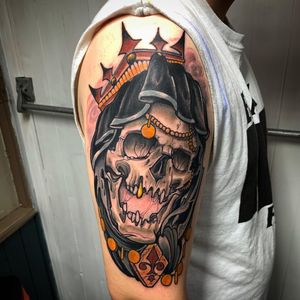 Illustrative upper arm tattoo featuring a skull wearing a golden crown, created by artist Jethro Wood.