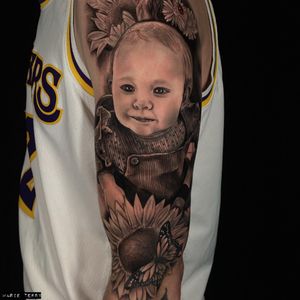 Incredible black and gray tattoo featuring a baby and a detailed flower, expertly done by artist Marie Terry.