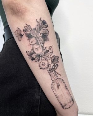Unique illustrative forearm tattoo featuring a flower blooming from a bottle, done by artist Anna.