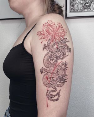 Get a stunning illustrative tattoo of a fierce dragon intertwined with delicate flowers on your upper arm by the talented artist Anna.