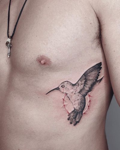 Elegant blackwork design by Anna on ribs depicting a stunning hummingbird surrounded by intricate thorns.