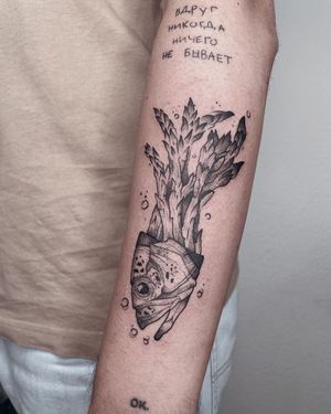 Unique upper arm tattoo by Anna featuring a mix of fish and vegetable motifs in blackwork style lettering and illustration.