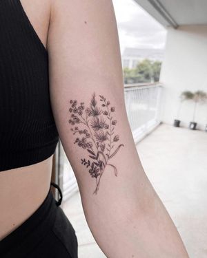 Beautiful upper arm tattoo by Alisa Hotlib featuring a delicate and intricate flower sprig design in fine line illustrative style.