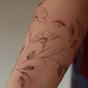 Beautiful fine line illustrative flower tattoo on the upper arm by talented artist Alisa.