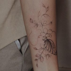 Small lettering adds a personal touch to this beautiful blackwork forearm tattoo showcasing an illustrative flower design and a name. Perfect for anyone looking for a delicate and meaningful piece.