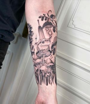 Adorn your forearm with a charming blackwork, fine line, and illustrative tattoo featuring a frog, flower, and mushroom design by talented artist Kasia.