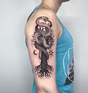 Beautifully bold upper arm tattoo featuring a striking combination of sun, moon, snake, and tree motifs, expertly done by Kasia.