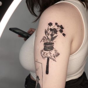 Beautiful blackwork upper arm tattoo featuring a delicate flower vase design by Mané.