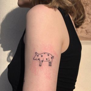 Unique illustrative tattoo on upper arm by artist Karyna, featuring a heart and a pig in a fine line blackwork style.