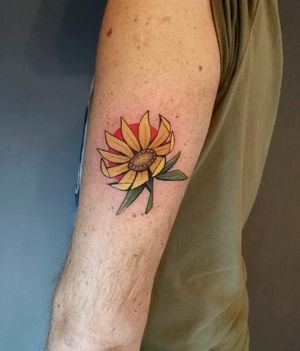 Get a vibrant and colorful sunflower tattoo on your upper arm with an illustrative style by tattoo artist Baingio.